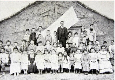 Maestros y niños posando frente a su escuela para una foto grupal.