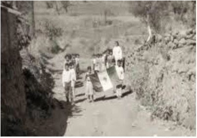 Niños en el campo desfilando como escolta con la bandera nacional mexicana.